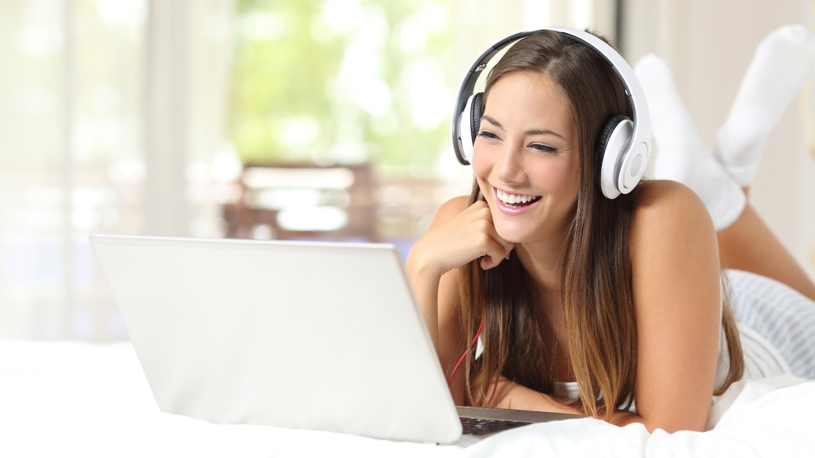 Girl with headphones reading in a laptop at home